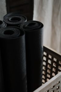 Close-up view of black yoga mats rolled and stacked in a wooden basket indoors.